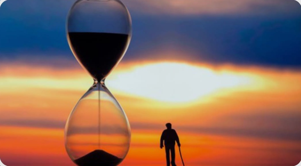 An hourglass silhouetted against a sunset sky, with a lone figure walking into the distance.